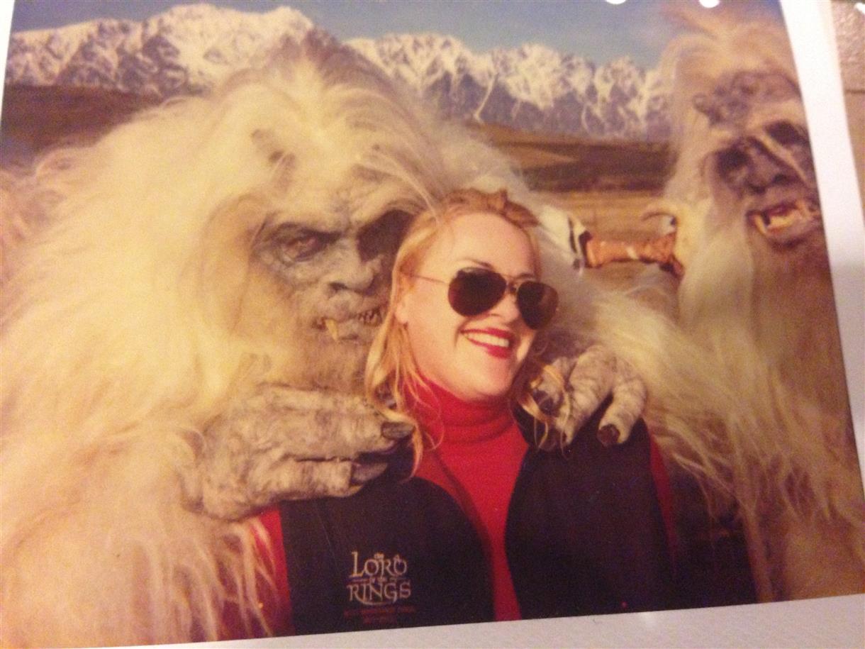 Gail Wilson on the Lord of the Rings set in New Zealand, wearing a LOTR cast vest, with creature characters and the Remarkables mountain range behind